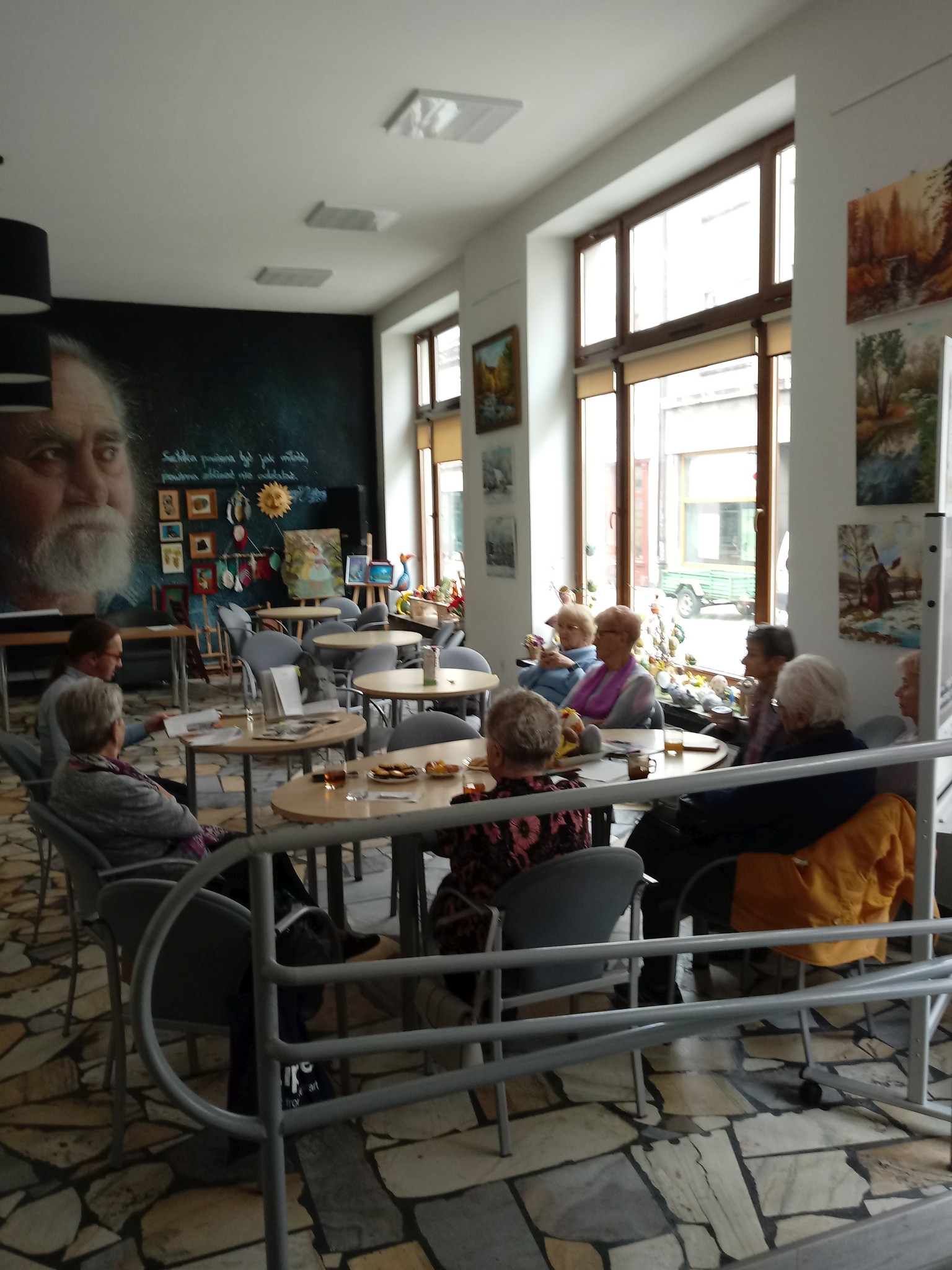 Sroda-z-ksiazka_20230419_1 W pomieszczeniu przy stolikach siedzi siedem osób. Mężczyzna prowadzi spotkanie.