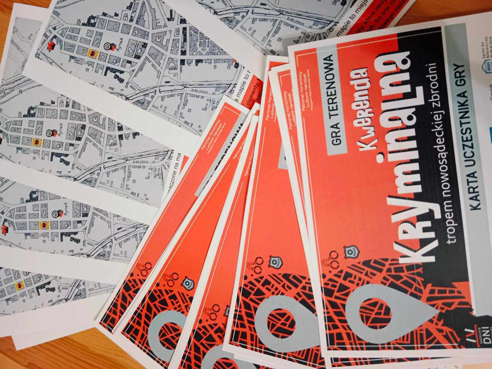 Po lewej stronie kilka map. Po prawej stronie ulotki. Na ulotkach napis Gra terenowa Kwerenda Kryminalna, tropem nowosądeckich zbrodni, Karta uczestnika gry.