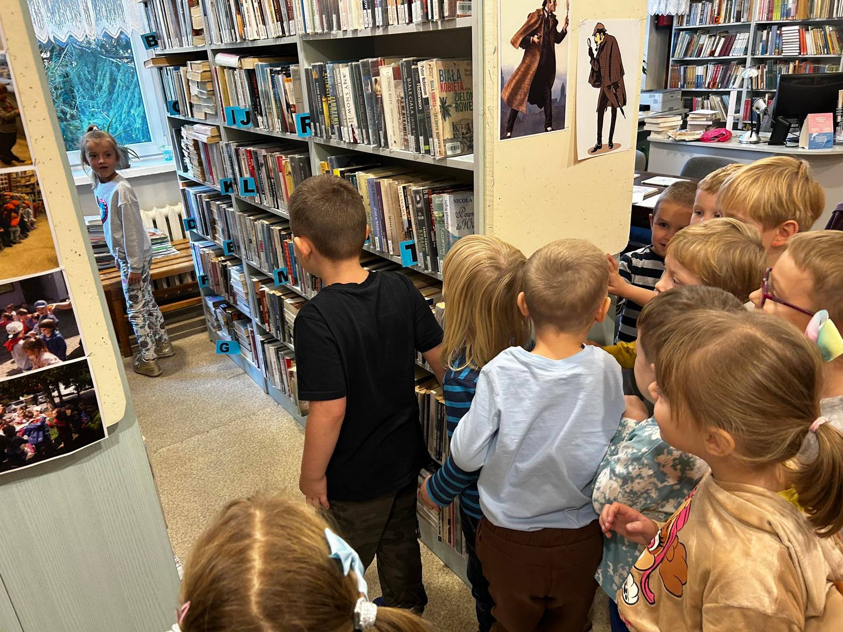 Detektyw Łodyga_5 Pokój wypełniony regałami z książkami. Pomiędzy regałami grupka dzieci.