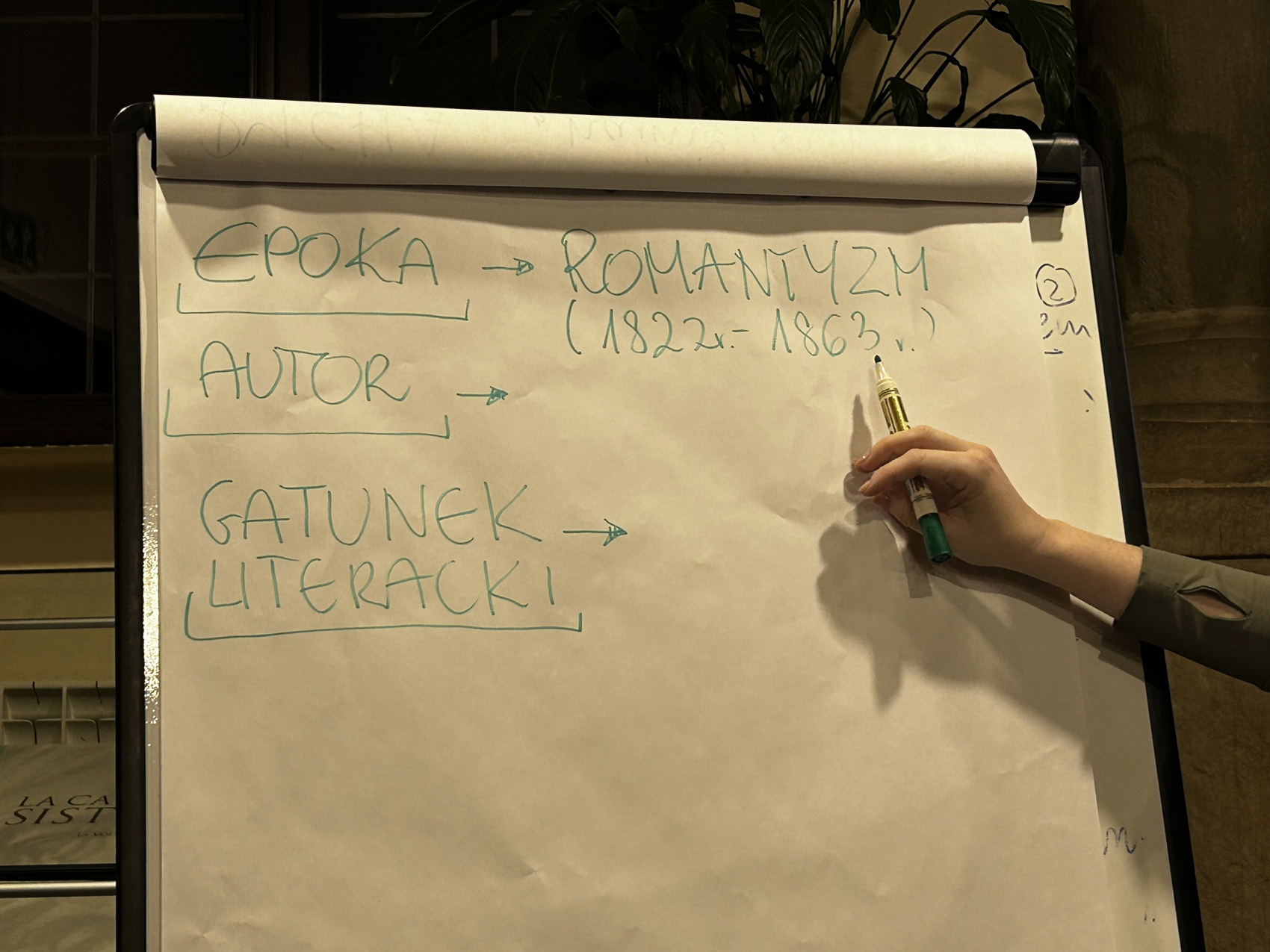 Egzamin 8klasisty – dziady ii (1) Flipchart. Na flipcharcie napisy: "Epoka - romantyzm 1822-1863, autor, gatunek literacki". Po prawej stronie flipchartu widać kobiecą rękę, trzymającą pisak. Ręka wskazuje pisakiem na datę.