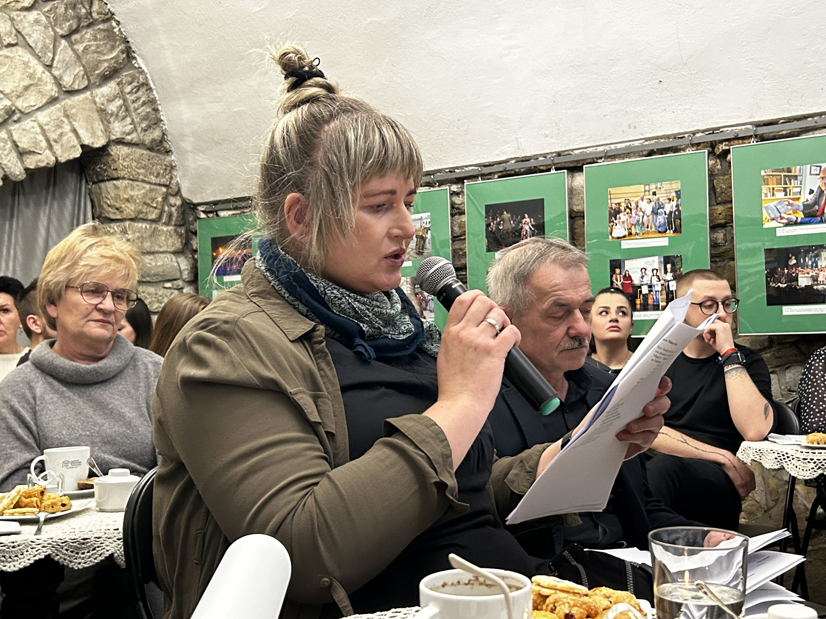 Wieczór wspomnień o Marii Piniańskiej (6) Kobieta czyta poezję Marii Piniańskiej, pozostali uczestnicy spotkania słuchają z uwagą.