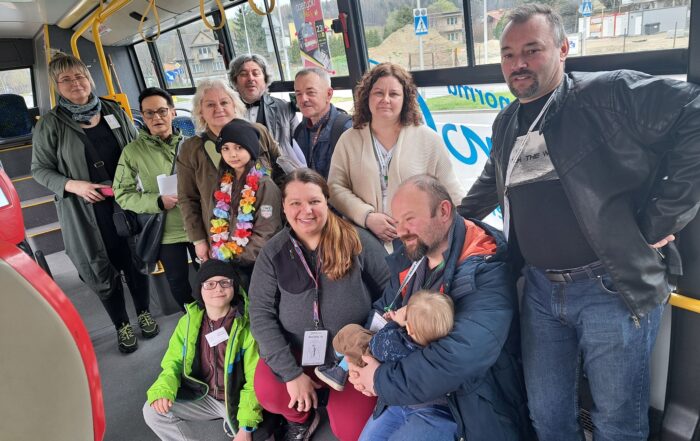 Autobus miejski. Grupa ludzi pozuje do zdjęcia. W tle przez szybę autobusu widać plac budowy, drzewa, domy.