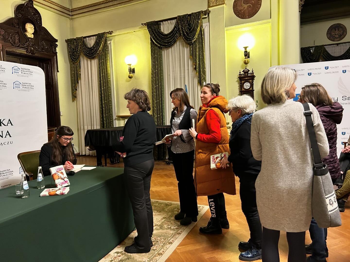 Małgorzata Lebda_6 Sala ratusza, po lewej stronie kobieta siedzi przy stole i podpisuje książkę. Przed nią kolejka kobiet czekających na podpis.