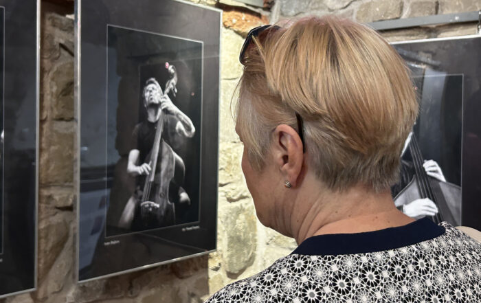 Kobieta w krótkich włosach przygląda się wiszącym na kamiennej ścianie czarno białej fotografii.