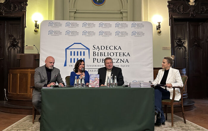 Cztery osoby siedzi przy stole. Jedna z kobiet mówi do mikrofonu.