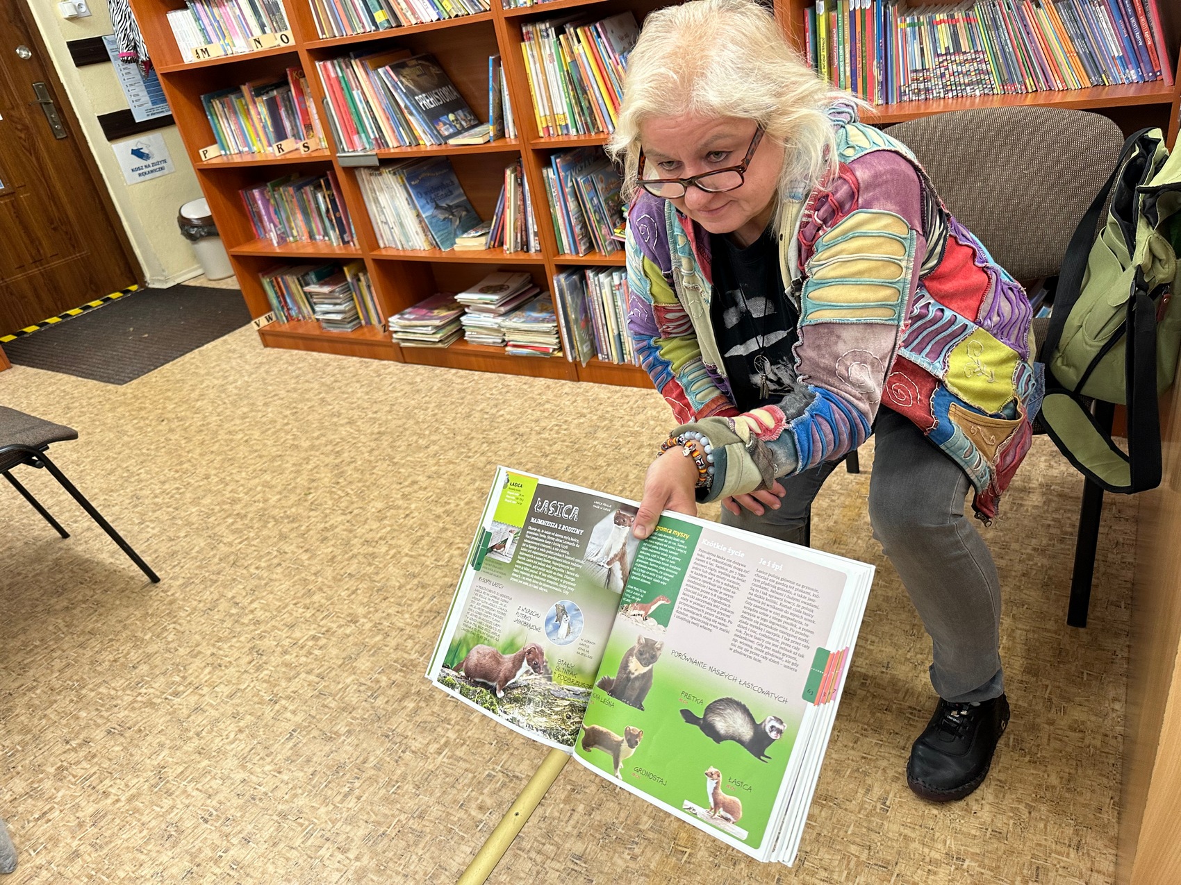 Sądeczanki_Babiarz_2 Kobieta w okularach siedzi w bibliotece i pokazuje książkę ze zwierzętami.