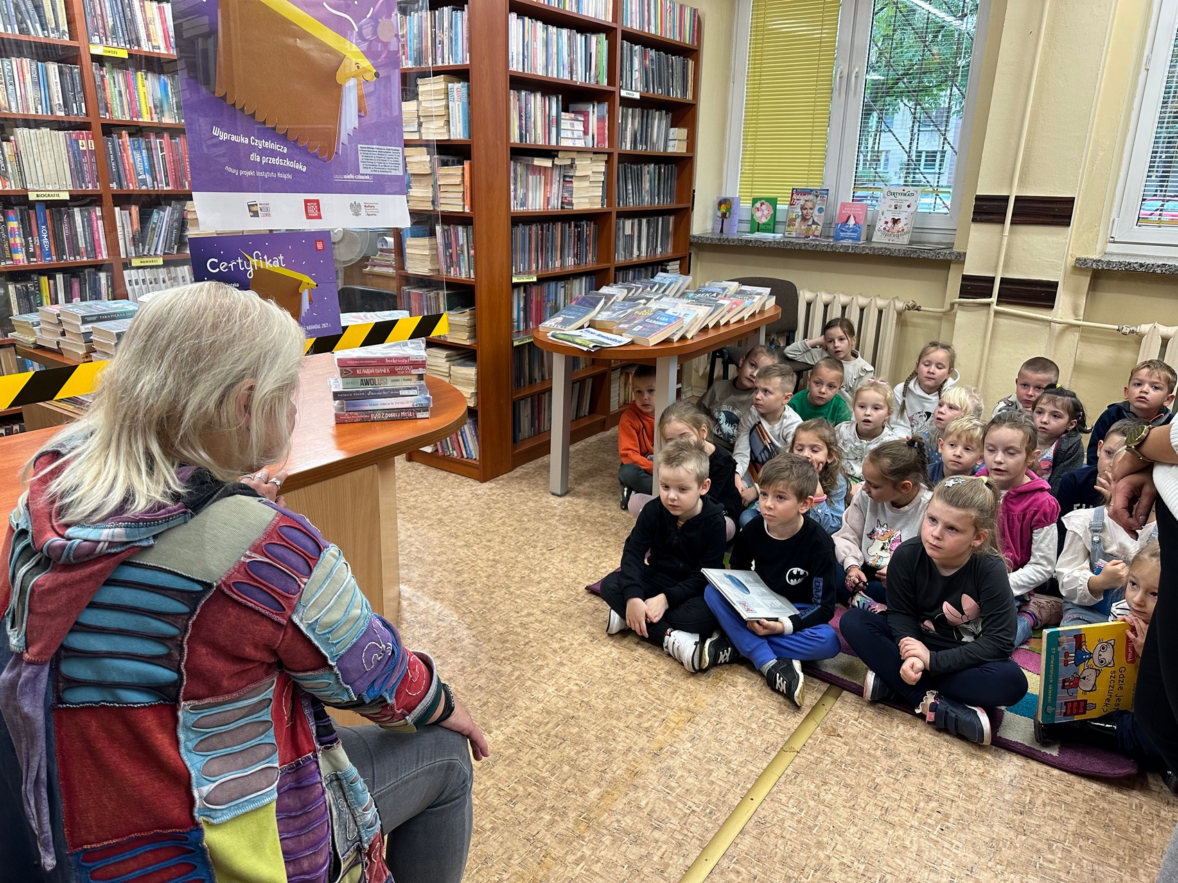Sądeczanki_Baiarz_3 Kobieta siedzi w bibliotece przed grupą małych dzieci.