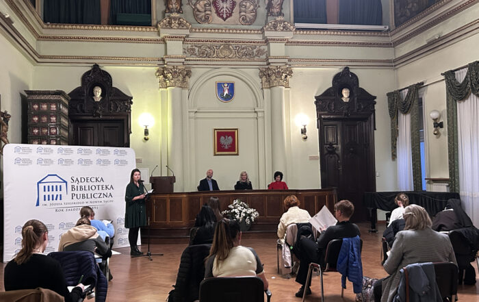 Sala ratuszowa, na której w sporych odstępach siedzą ludzie.