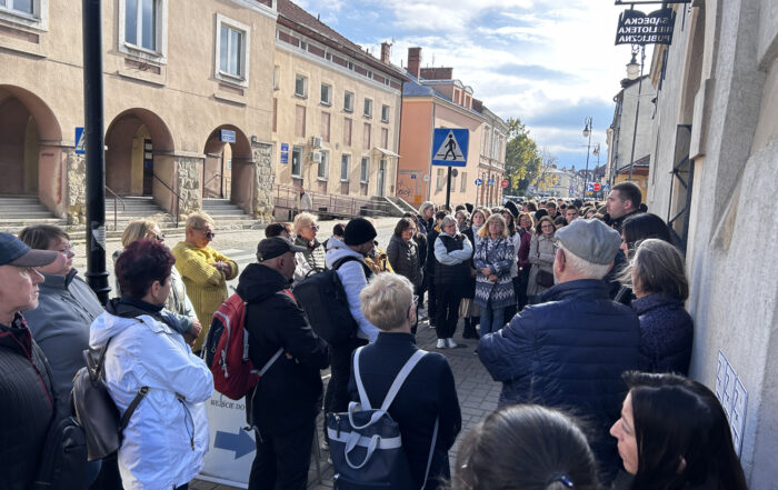Mężczyzna mówi do mikrofonu do grupy ludzi, która stoi na chodniku.