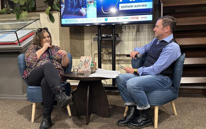 Dwie osoby siedzą na krzesłach przy stoliku i rozmawiają.