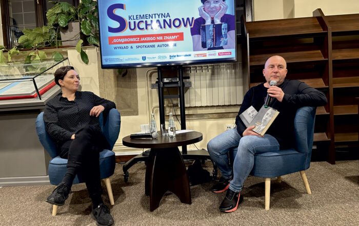 Kobieta i mężczyzna siedzą na krzesłach i opowiadają o książce. Pomiędzy nimi jest ekran.