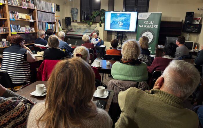 Grupa osób przysłuchuje się kobiecie z przodu sali.