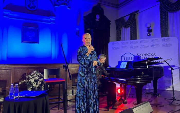 Kobieta śpiewa do mikrofonu. Obok niej na fortepianie gra mężczyzna.