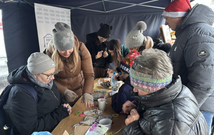 Grupa ludzi w zimowych ubraniach i w namiocie, która robi ozdoby z koralików.