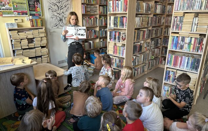 Dzieci siedzą na podłodze i patrzą się na kobietę z książką.