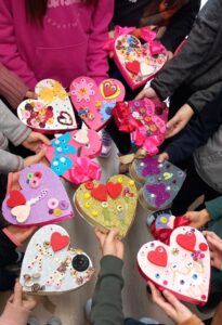 Dzieci trzymają w rękach dziesięć kolorowych laurek w kształcie serc.